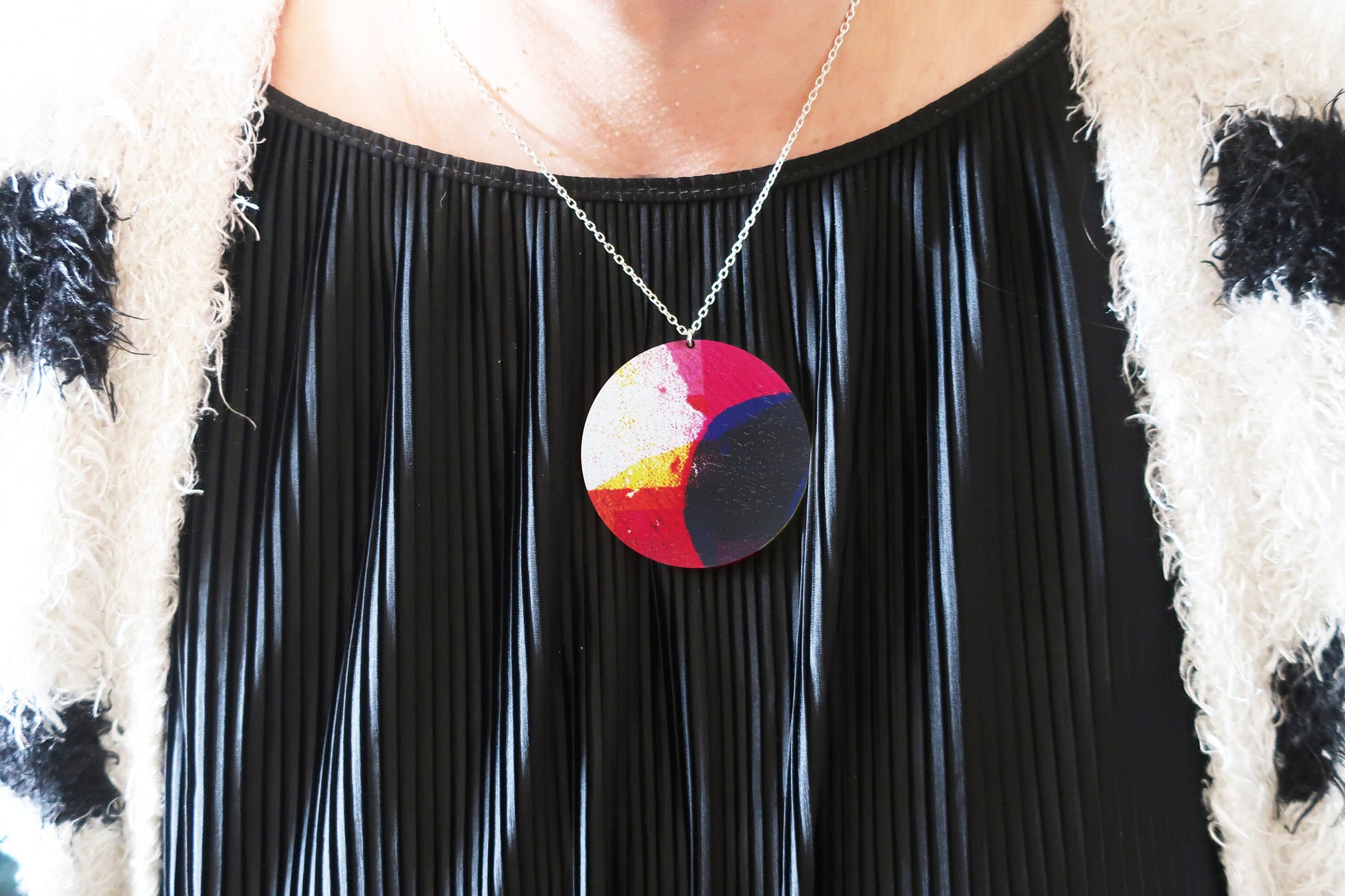 Person wearing a colorful pendant necklace with a black pleated top.