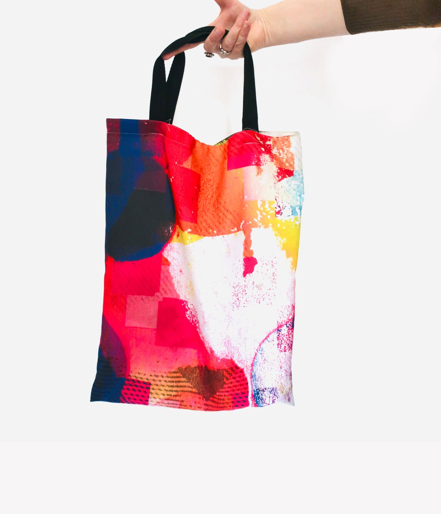 Colorful tote bag with abstract design held by a hand on a white background