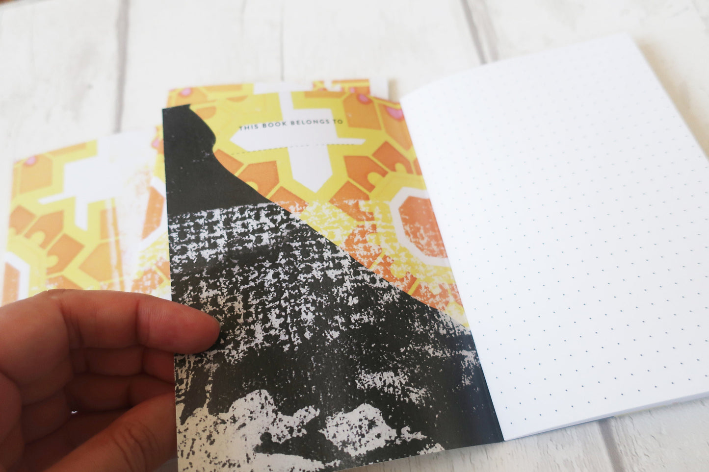 Book with abstract design held by a hand on a white surface