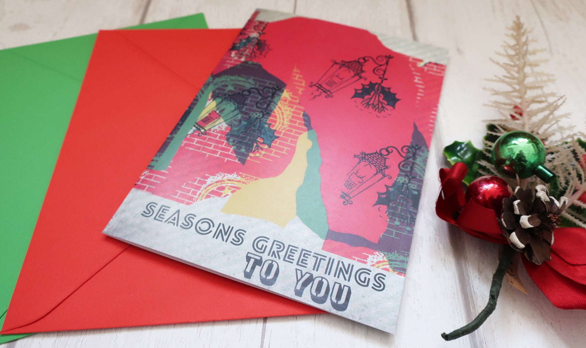 Seasons Greetings card with red envelope and Christmas decorations on a light background