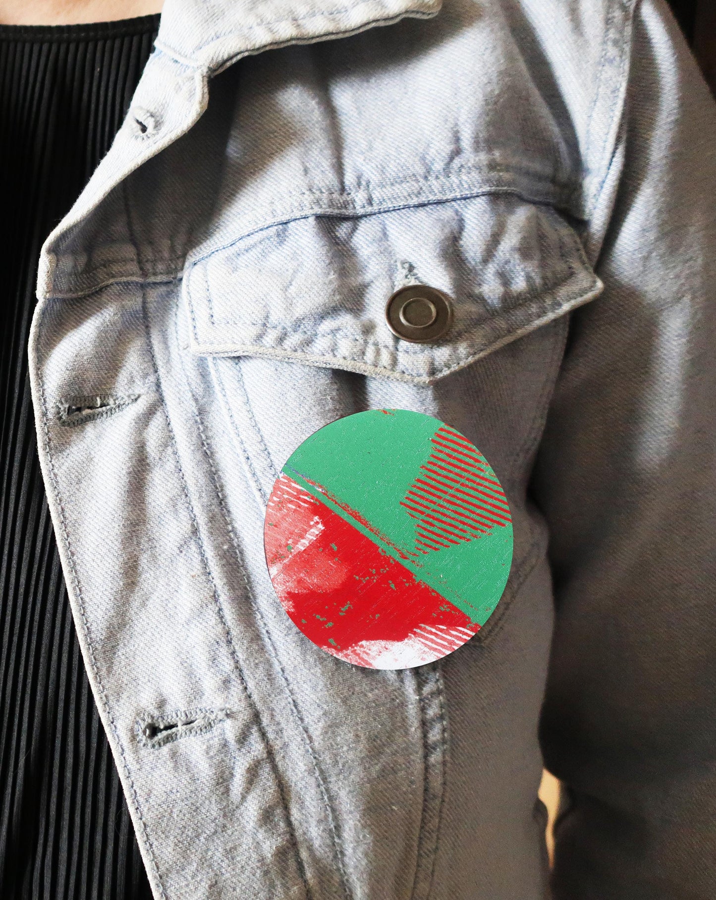 Round red and green brooch attached to a light gray jacket