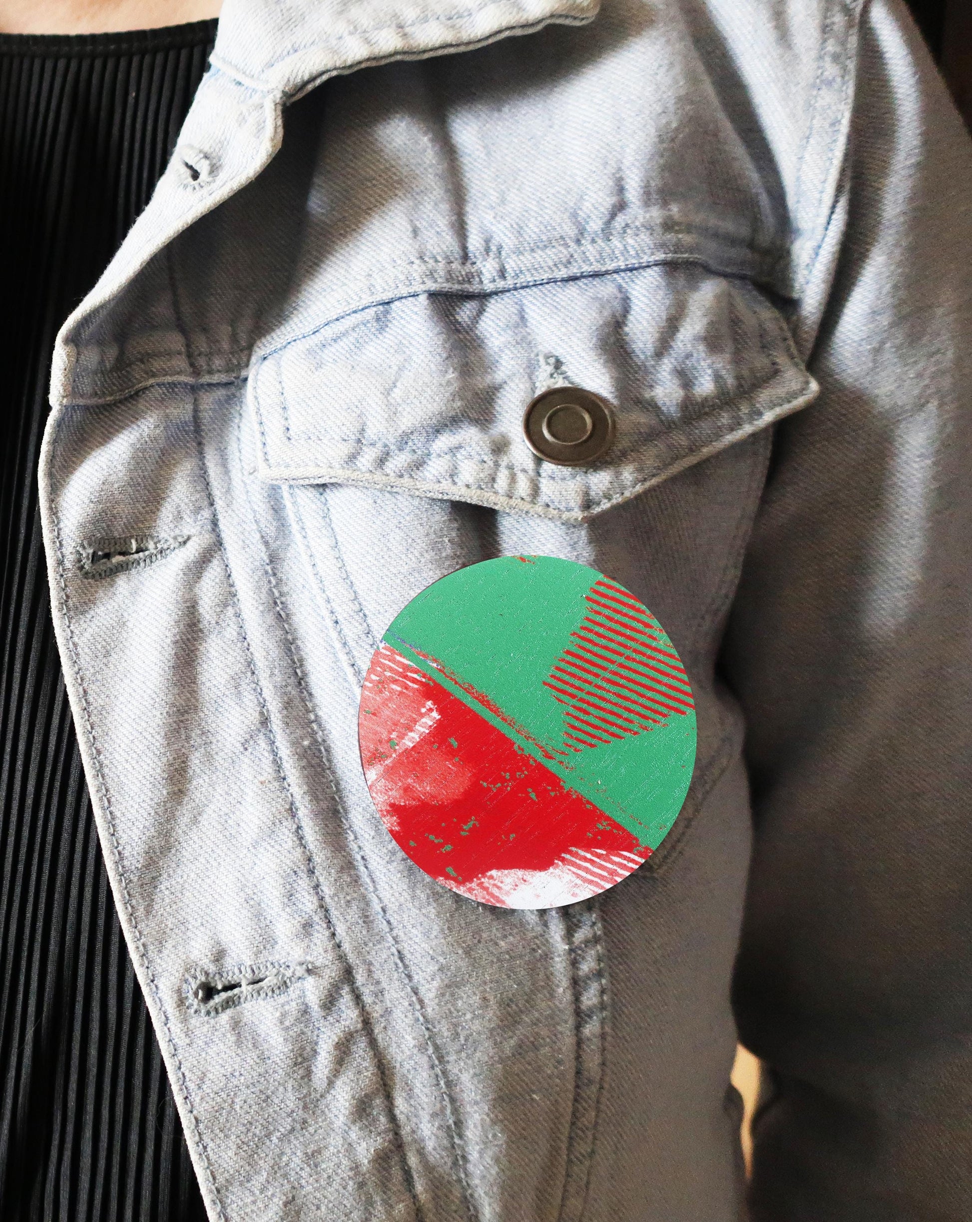 Round red and green brooch attached to a light gray jacket