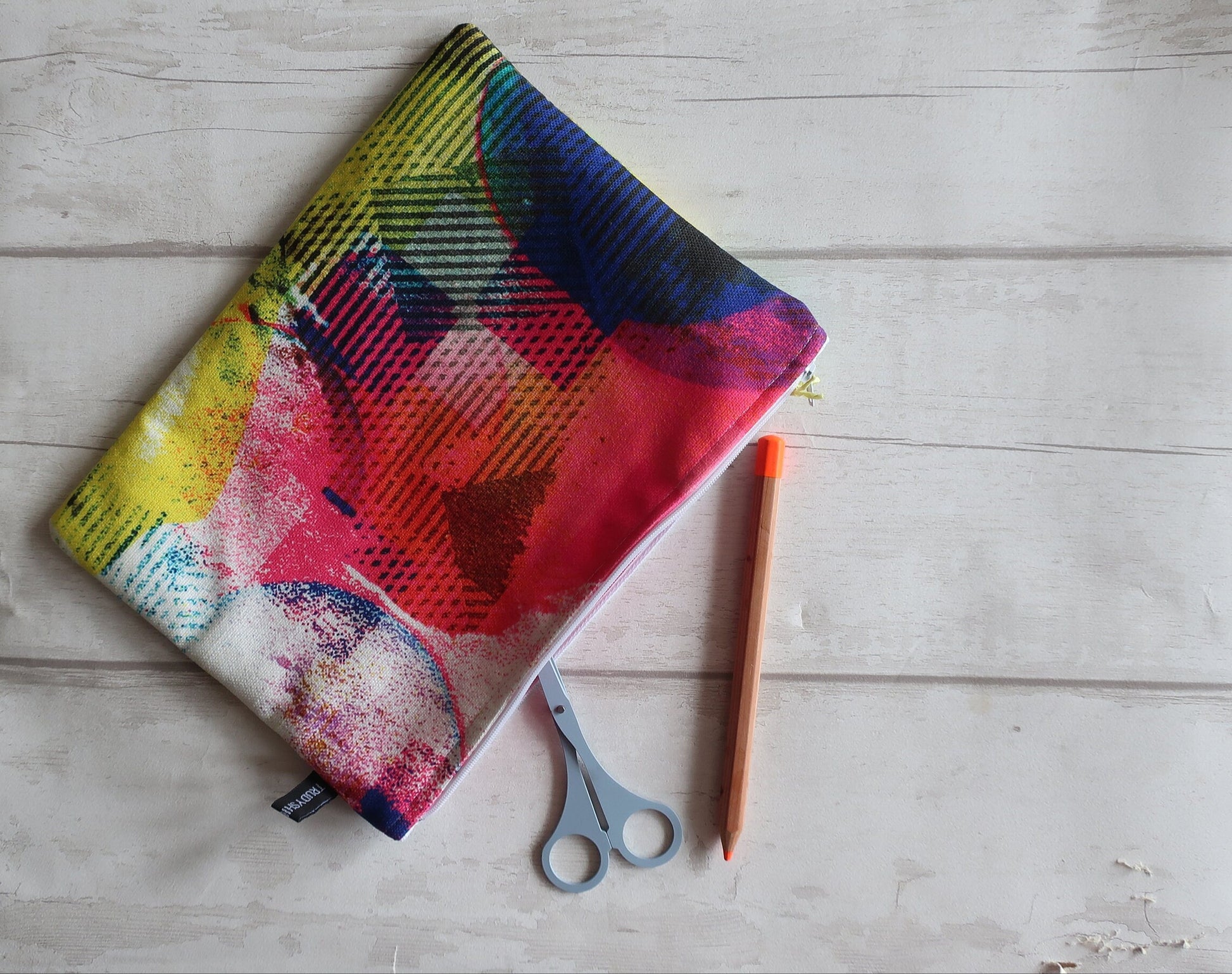 Colorful fabric with abstract patterns on a wooden surface with scissors and a pencil.