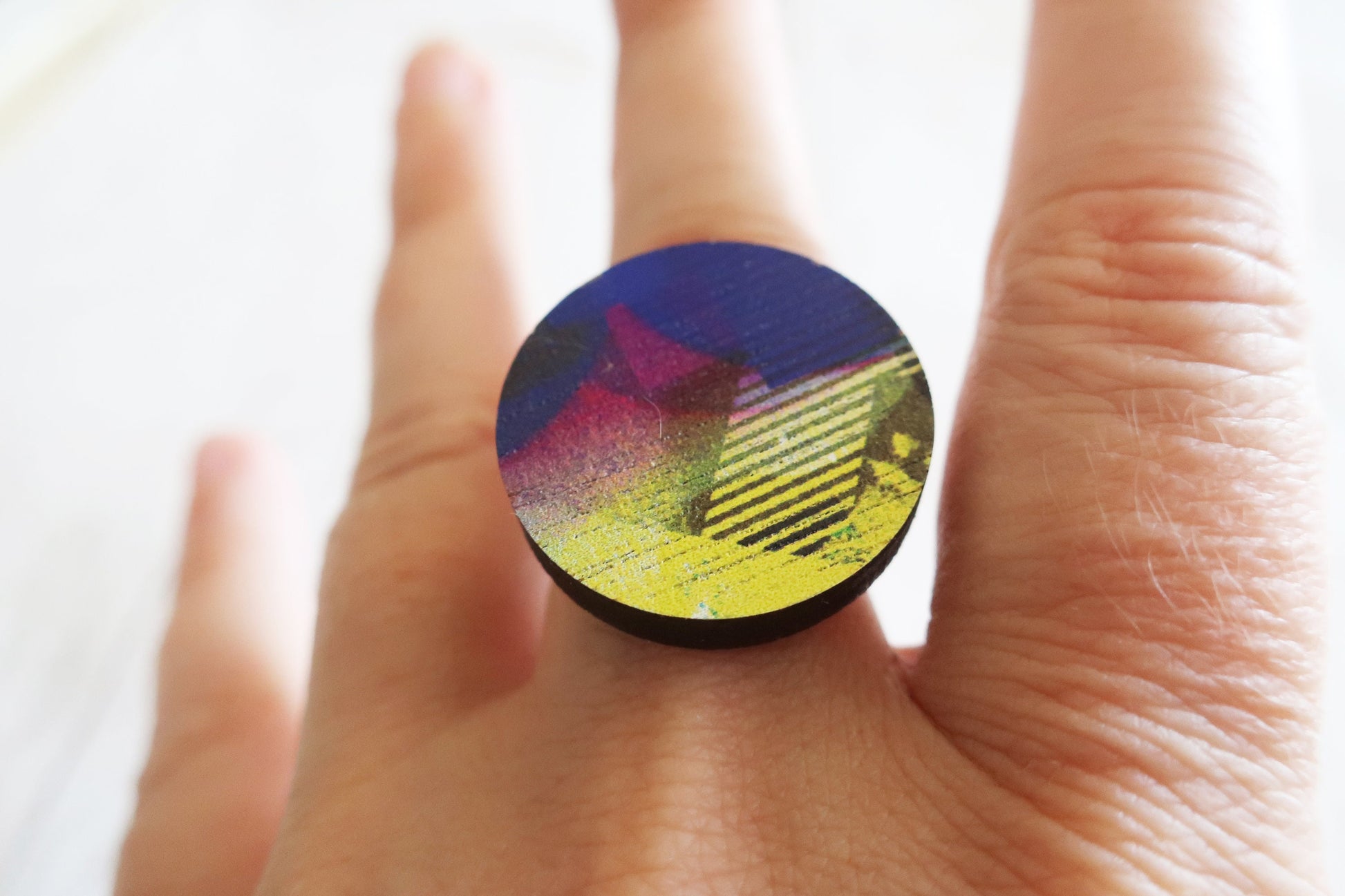Colorful ring with geometric design on a finger against a white background