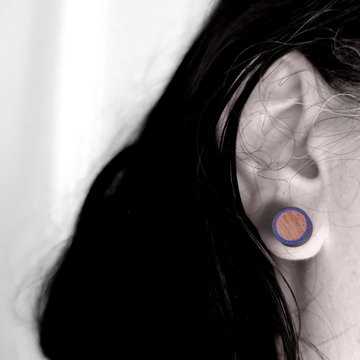 Close-up of an ear wearing a wooden earring with a blue circle on a neutral background