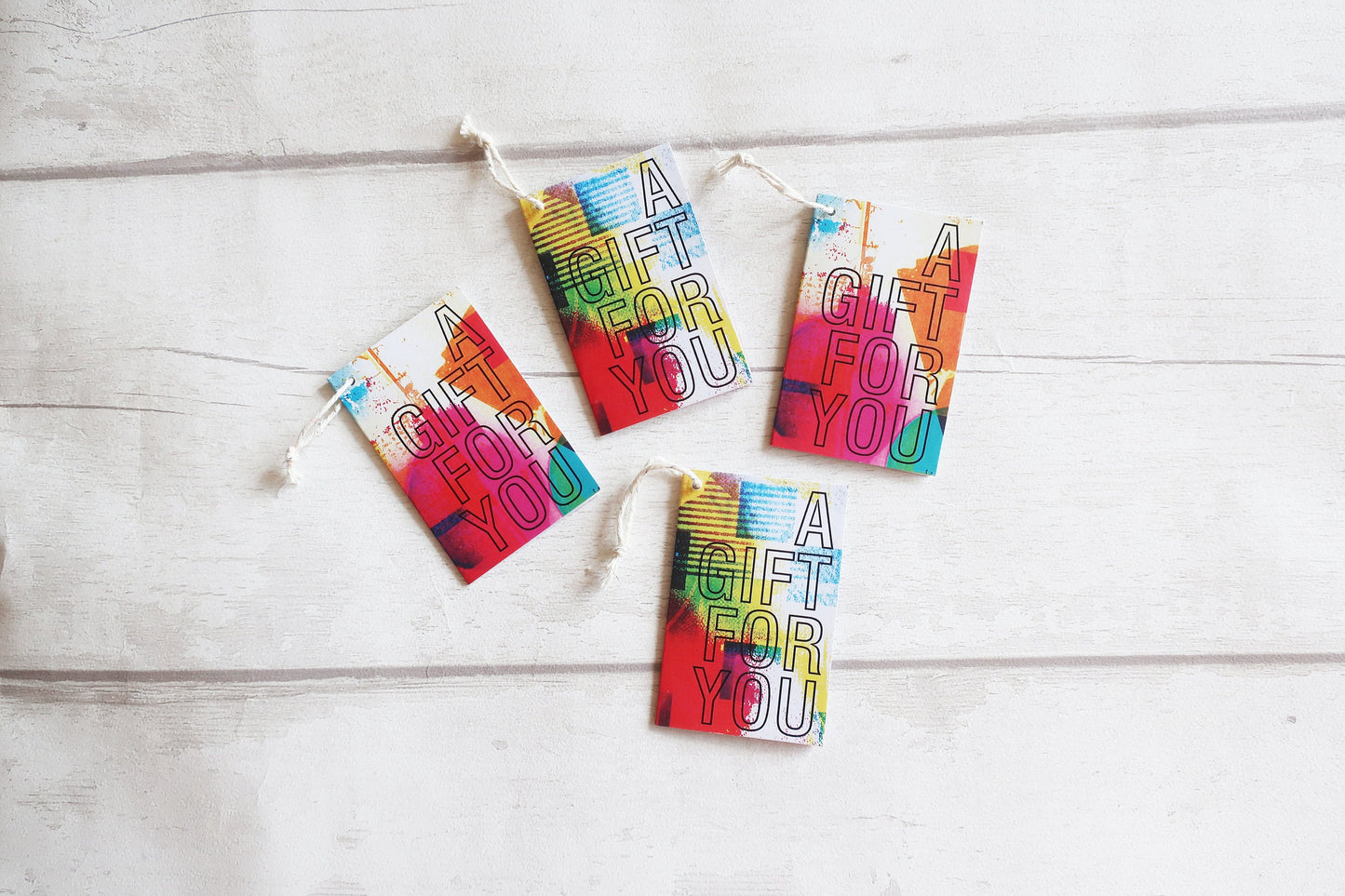 Four colorful 'A Gift For You' tags on a wooden surface