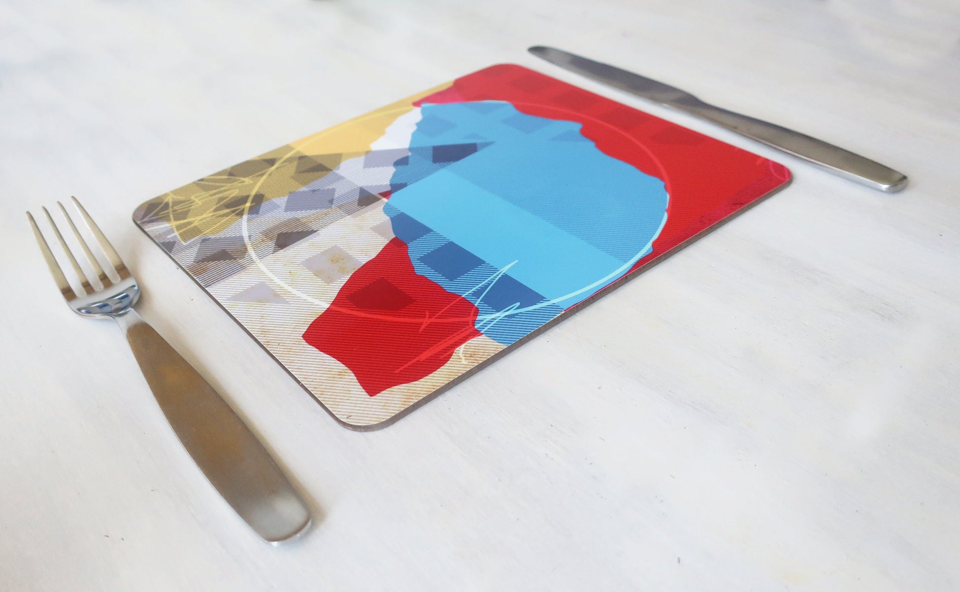 Colorful placemat with a blue and red design on a white tablecloth, accompanied by a fork and knife.