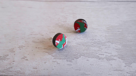 Pair of round earrings with red, green, and black design on a light wooden surface.