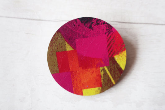 Colorful circular brooch with abstract design on a white background