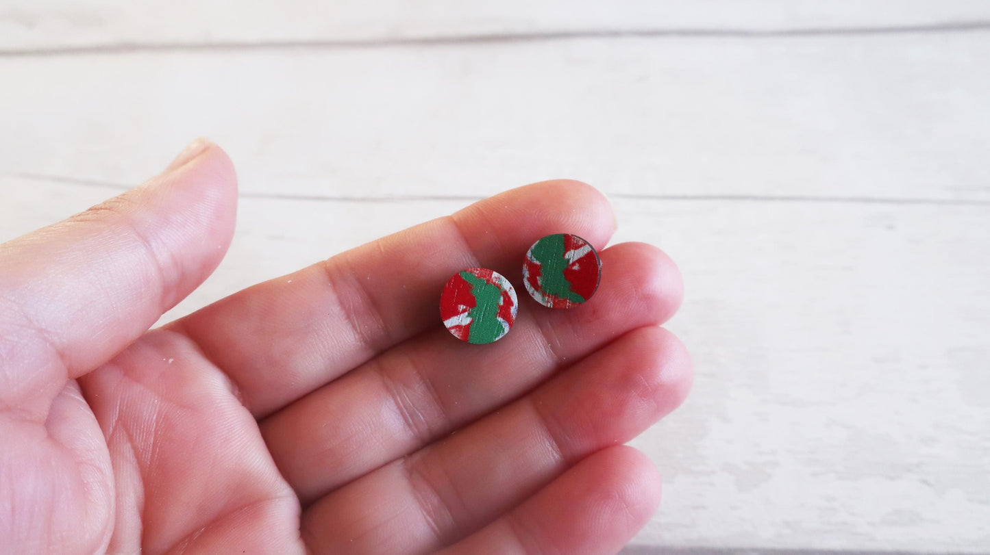 Small round earrings with red and green design held between fingers on a light background