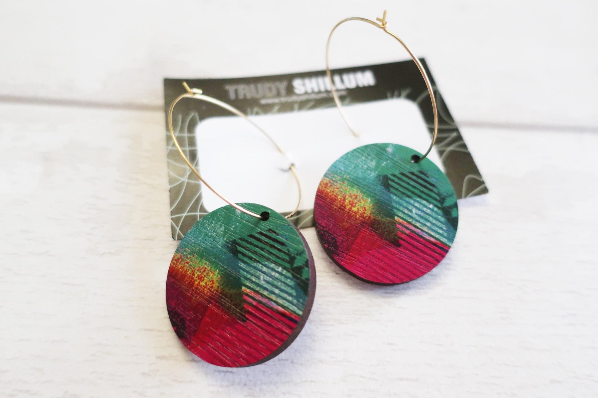 Colorful hoop earrings on a white background with a branded card behind them.