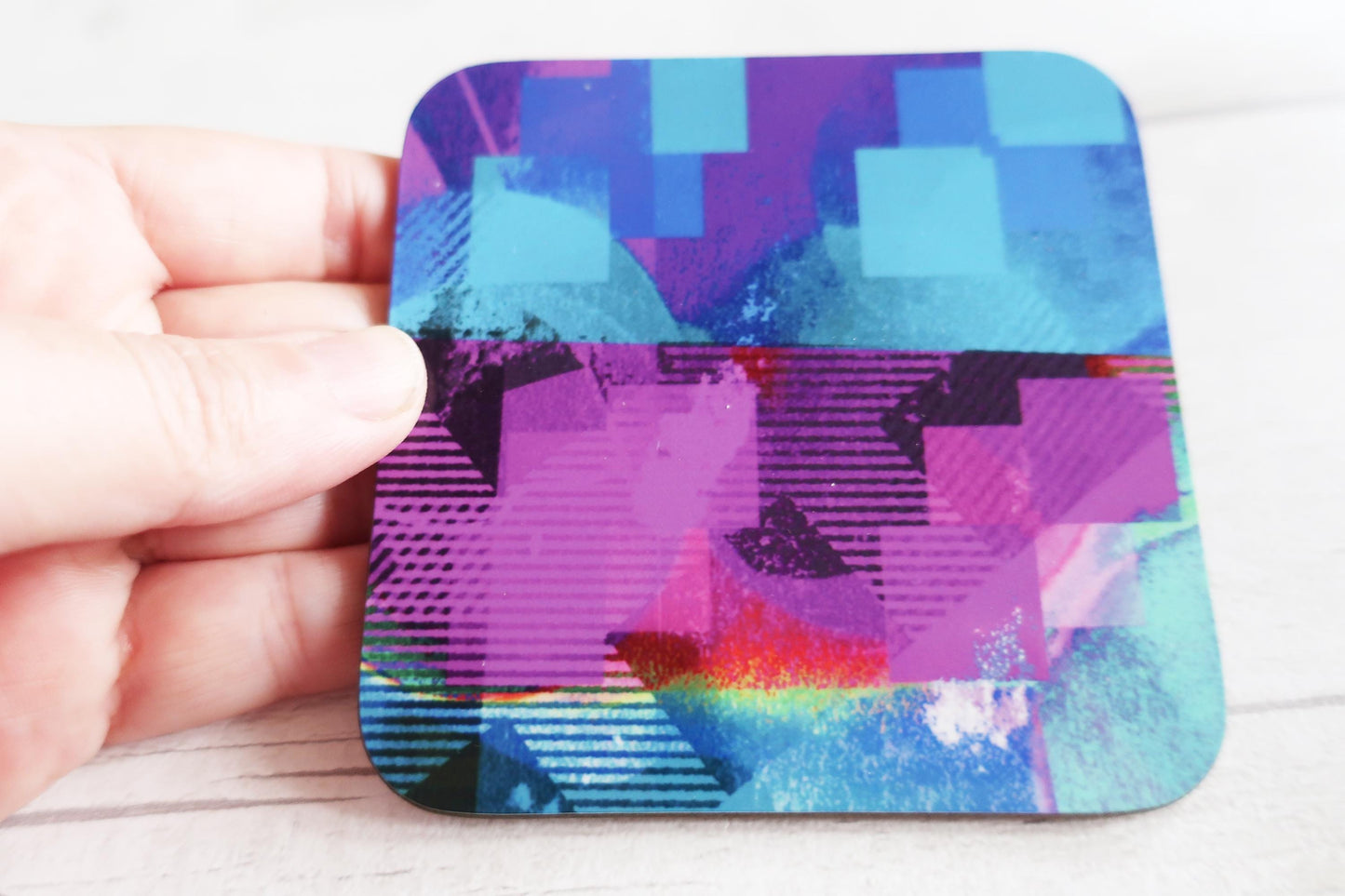 Colorful abstract coaster held by a hand on a light wooden surface