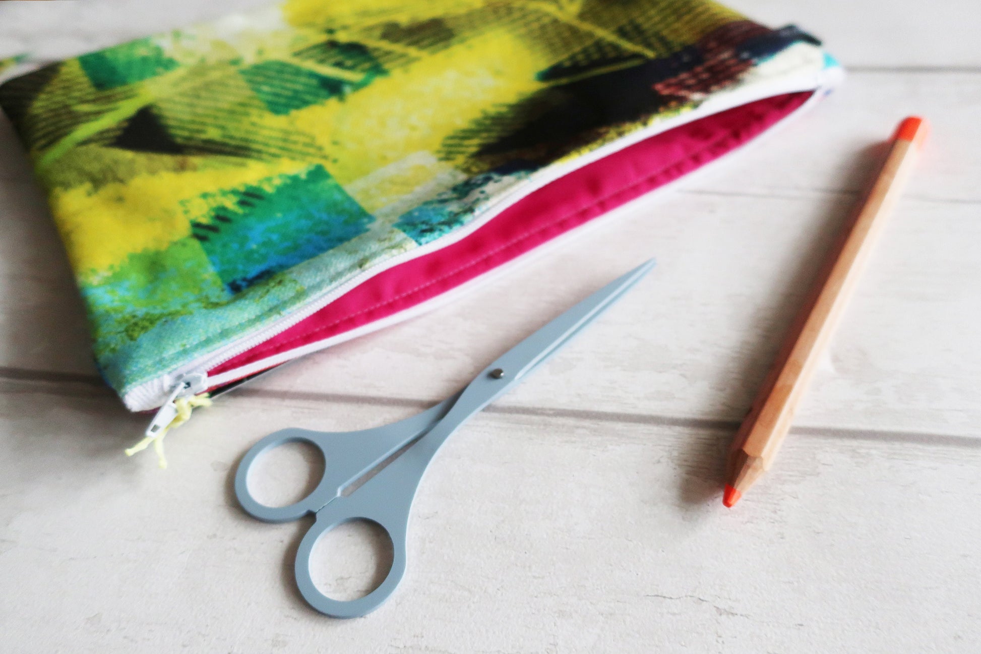 Colorful fabric pouch, scissors, and a pencil on a light wooden surface