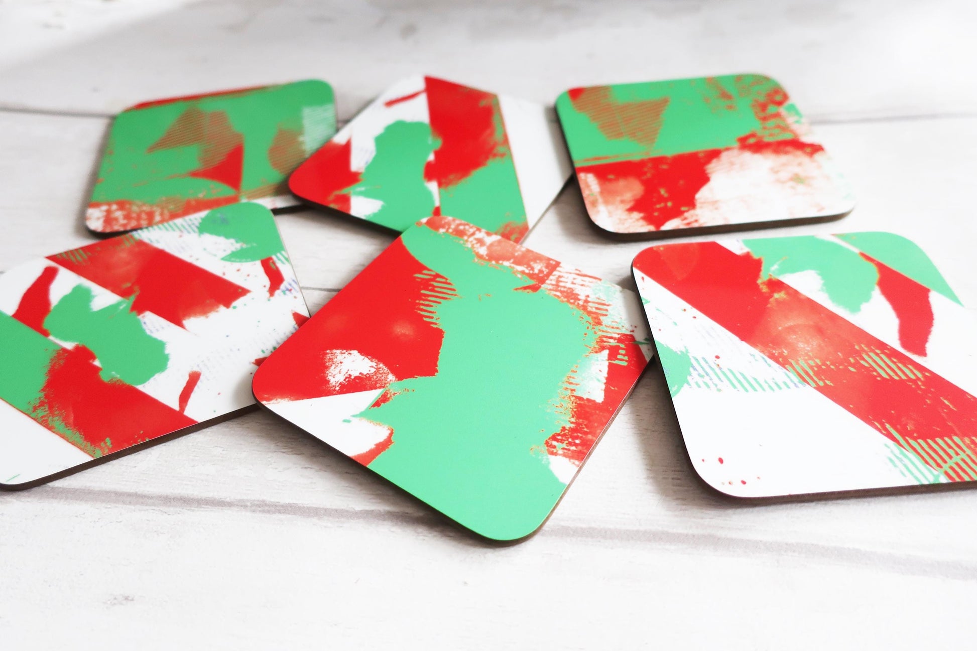 Set of geometric coasters with red, green, and white patterns on a wooden surface.