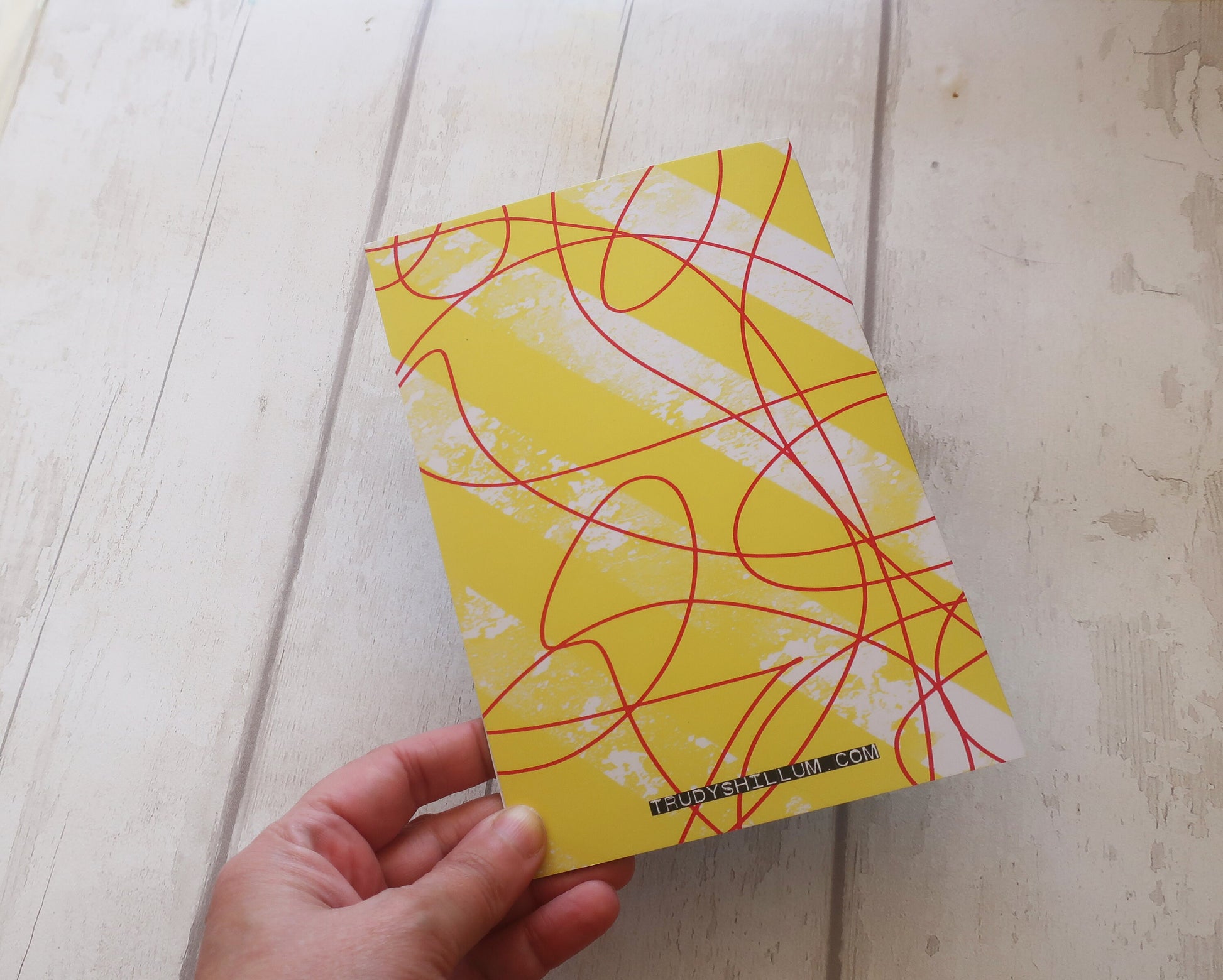 Yellow card back with red abstract patterns held by a hand on a light wooden surface