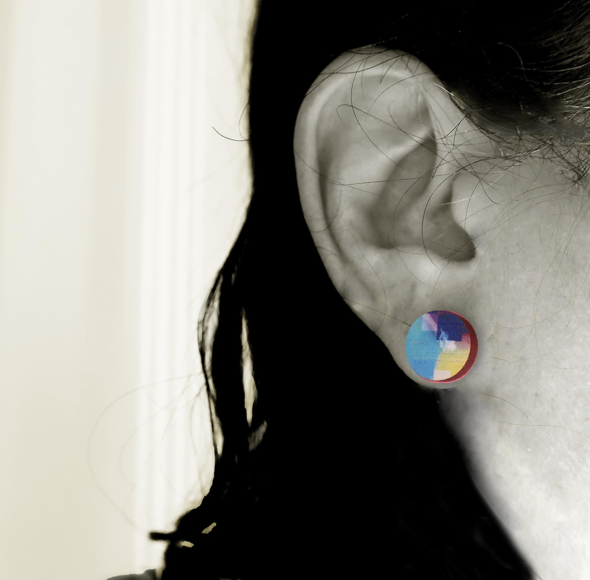 Close-up of an ear wearing a colorful circular earring with a blurred background