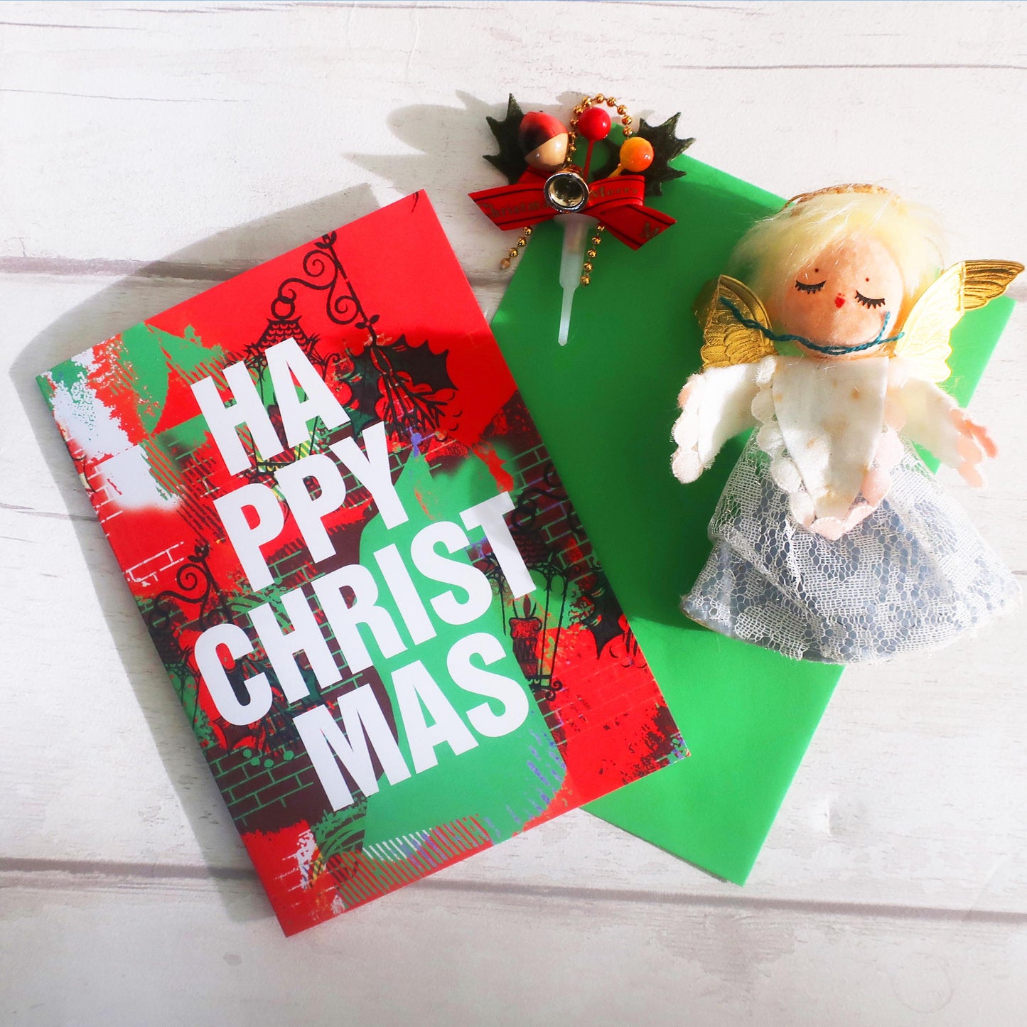 Christmas card with 'Happy Christmas' text, green envelope, and angel figurine on a white surface.