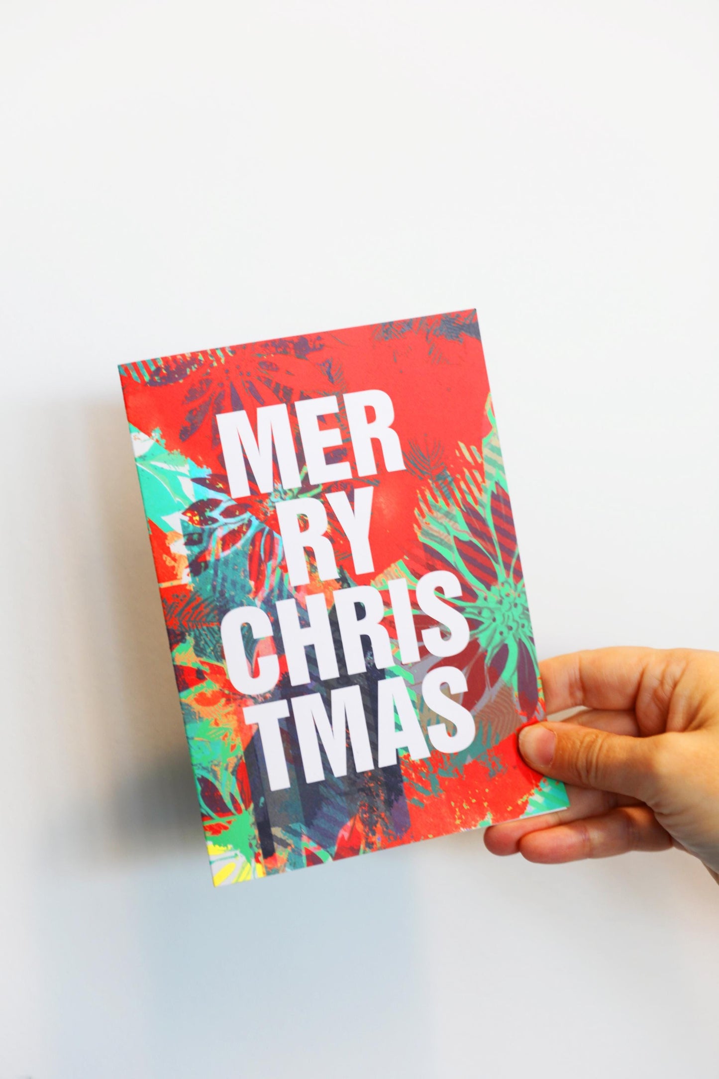 Hand holding a colorful Christmas card with 'Merry Christmas' text on a white background