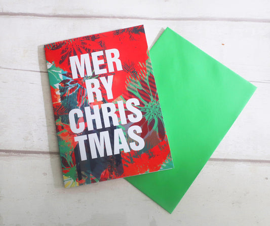 Christmas card with 'Merry Christmas' text and a green envelope on a white wooden surface