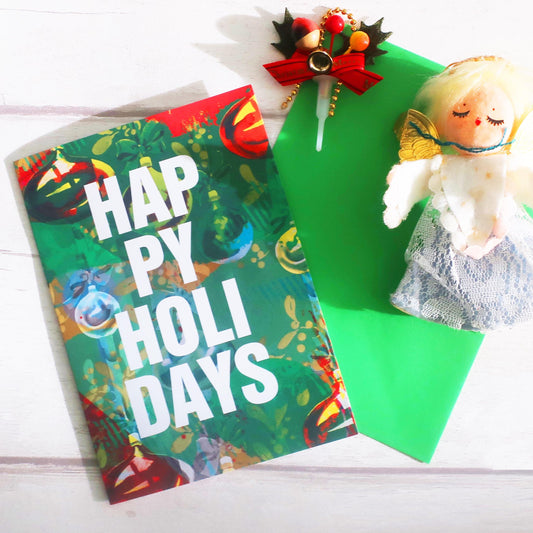 Colorful card with 'Happy Holidays' text, green paper, and decorative items on a white surface.
