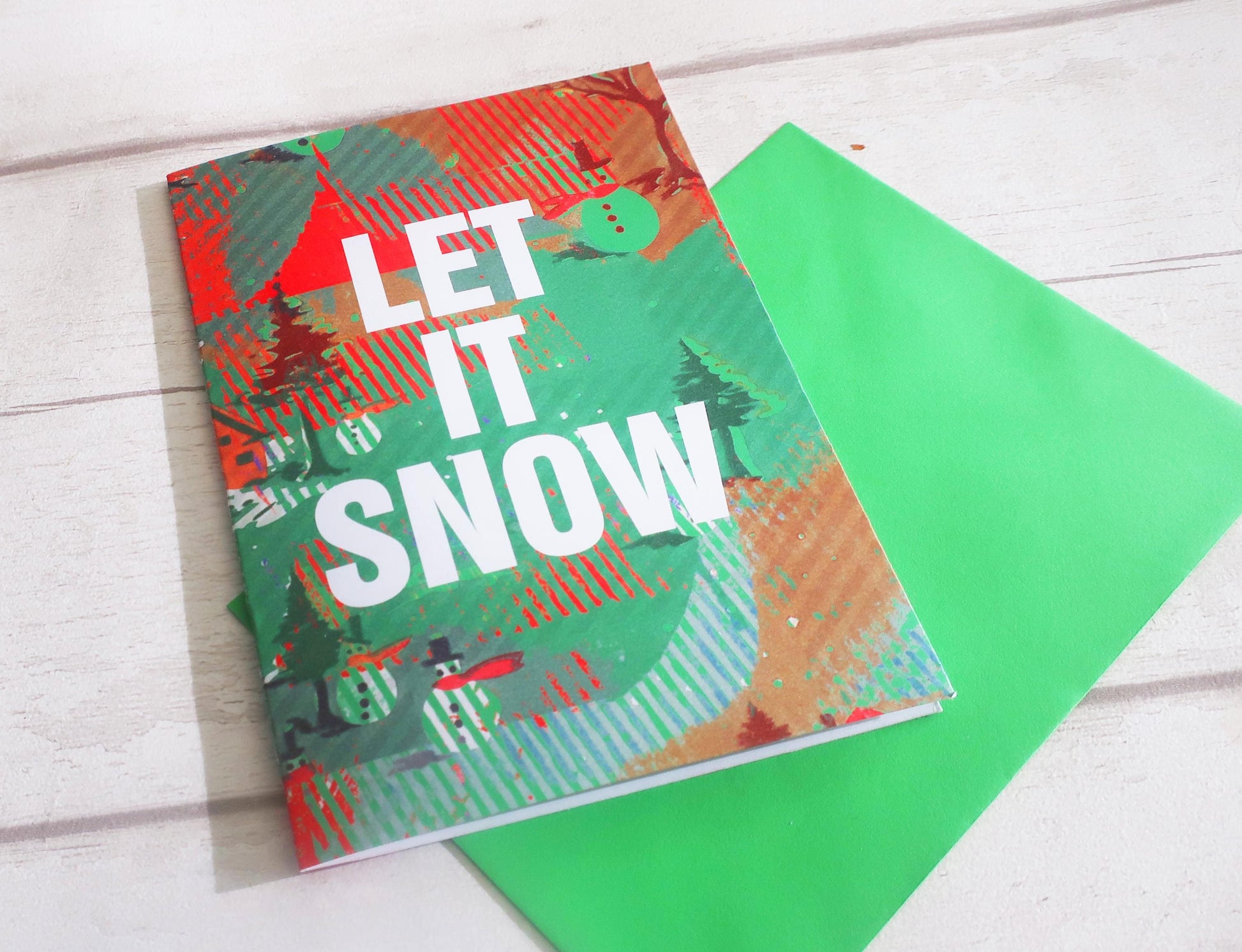 Holiday card with 'Let It Snow' text and colorful design on a green envelope.