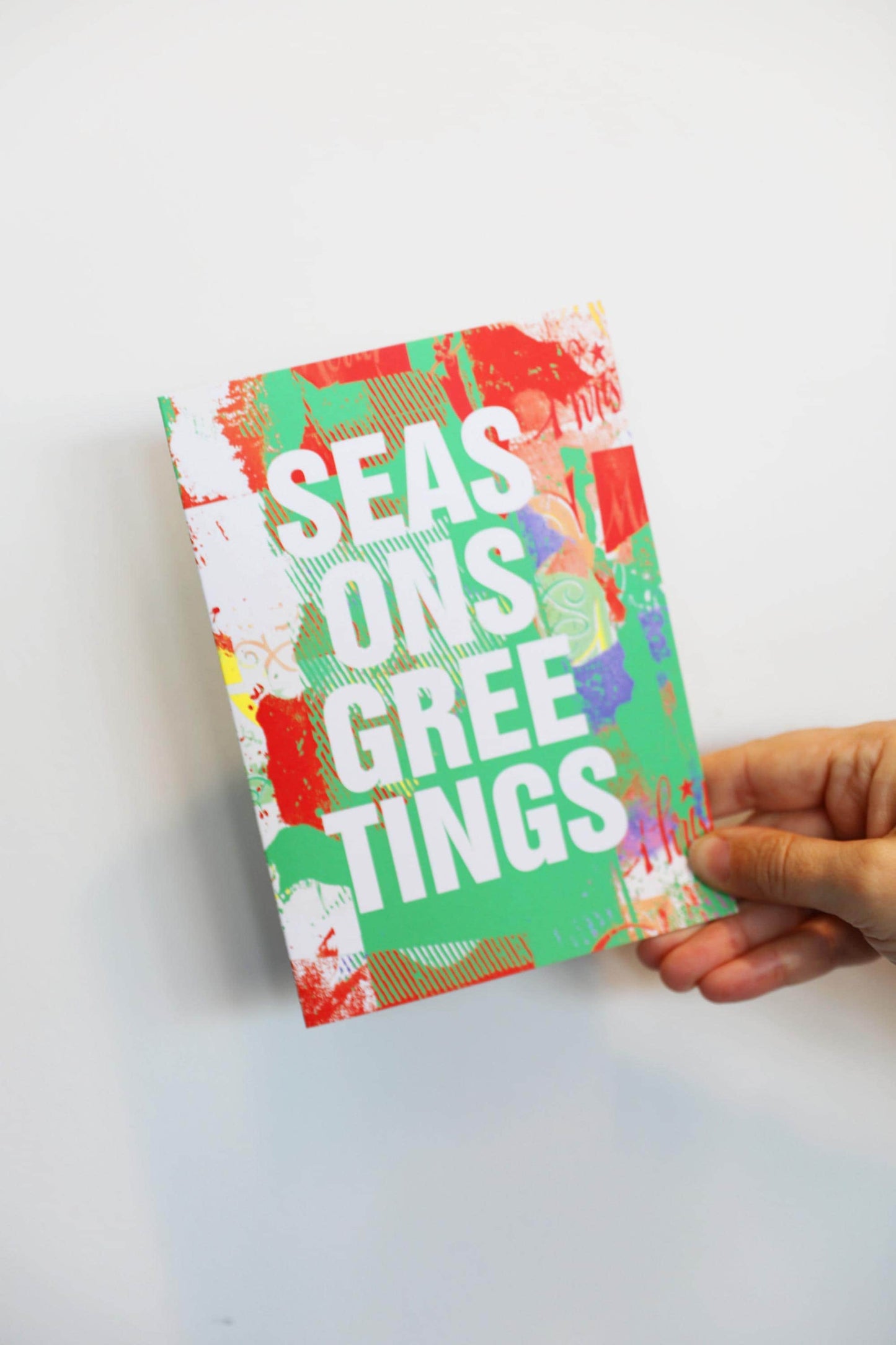 Hand holding a colorful 'Seasons Greetings' card on a white background