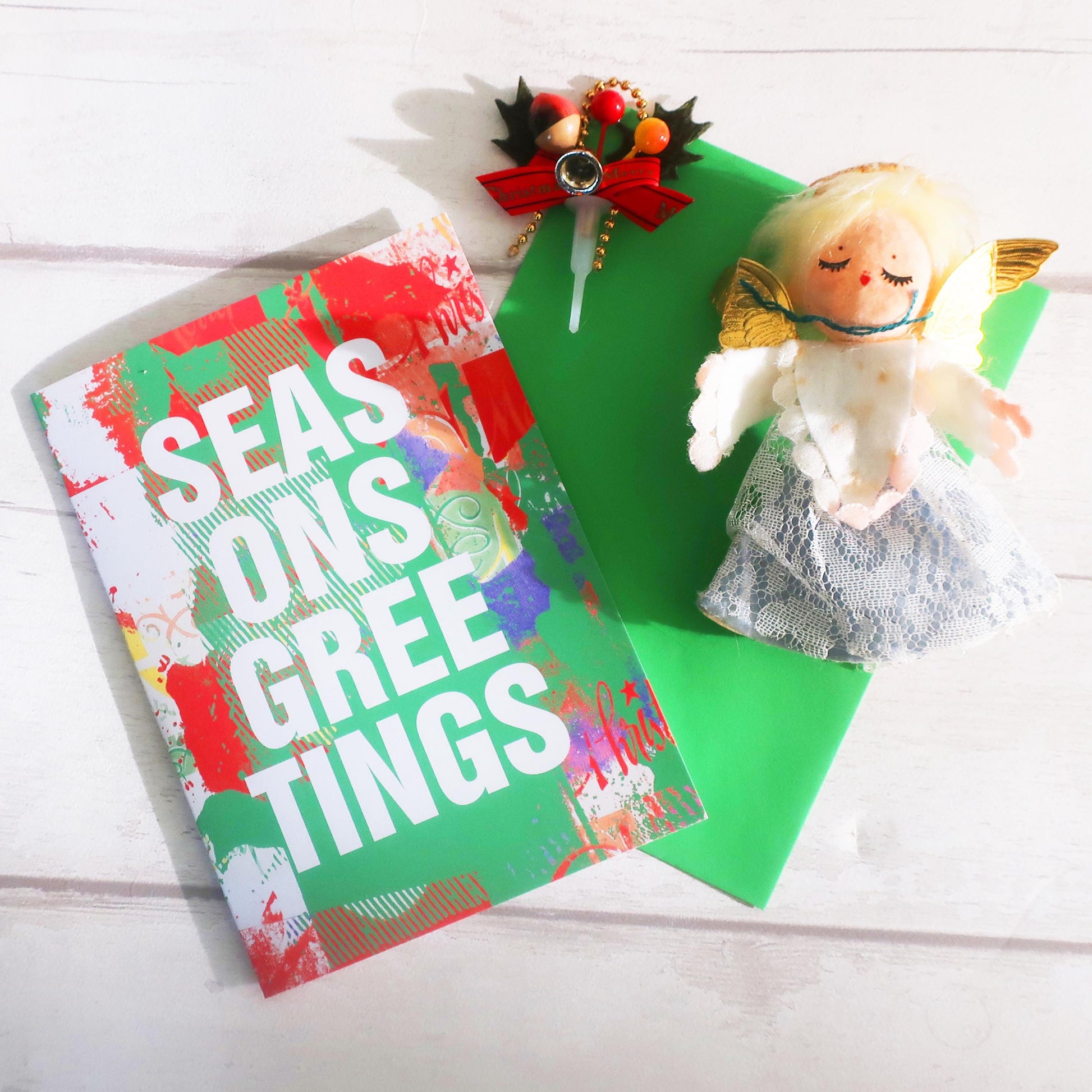 Christmas card with 'Season's Greetings' text, decorative bow, and angel figurine on a white background.