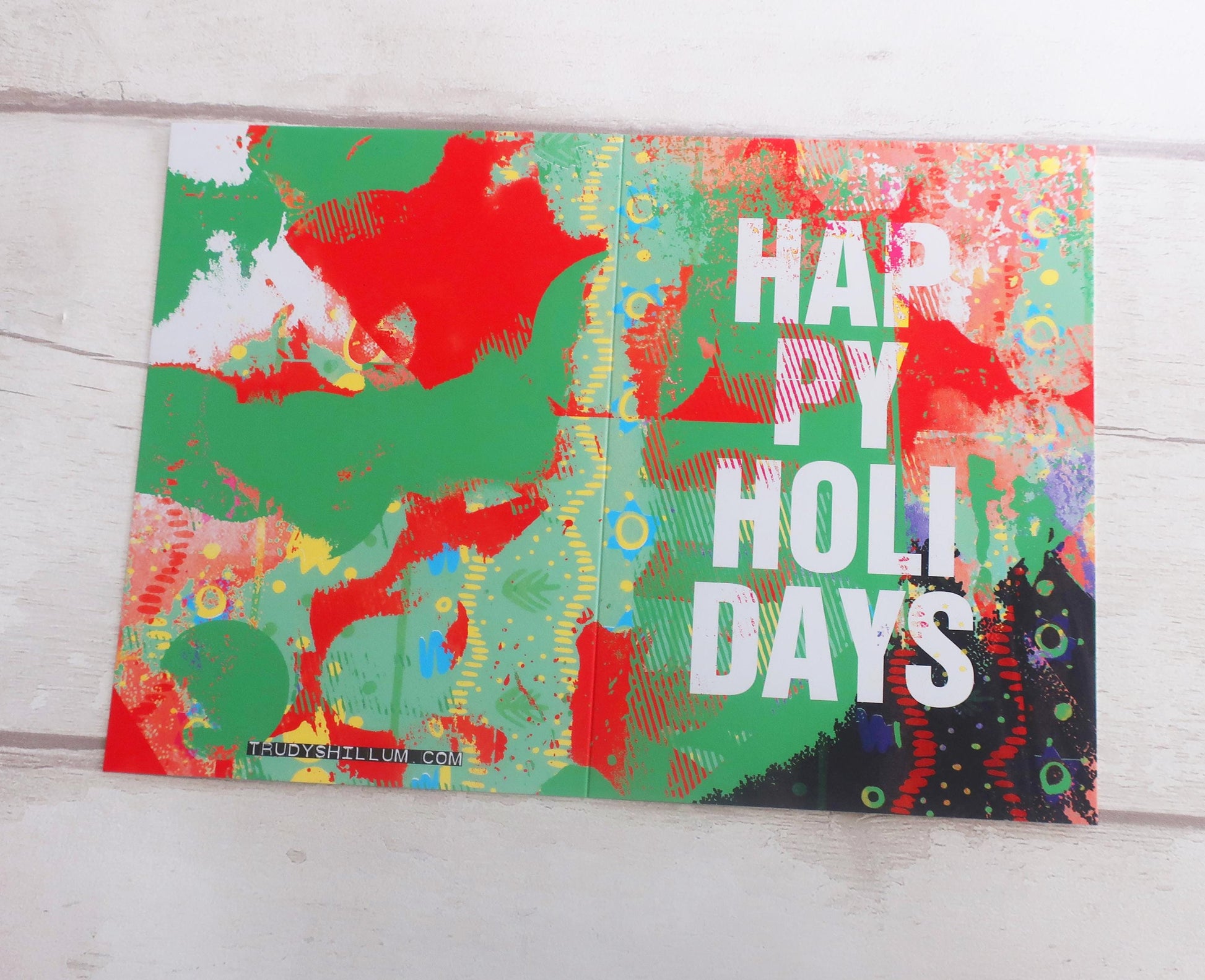 Colorful holiday card with 'Happy Holly Days' text on a wooden surface