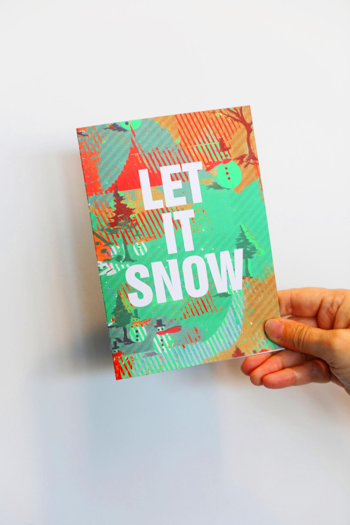 Hand holding a colorful card with 'LET IT SNOW!' text on a white background