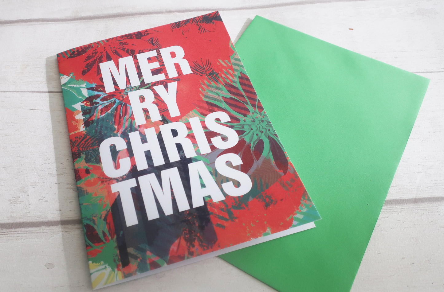 Colorful Christmas-themed card with 'Merry Christmas' text on a white wooden surface