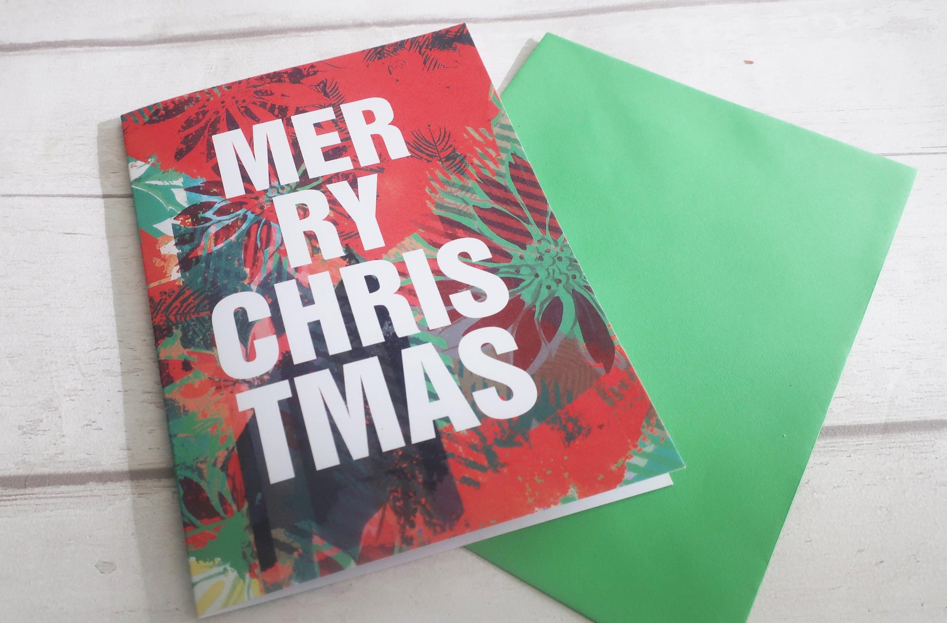 Colorful Christmas-themed card with 'Merry Christmas' text on a white wooden surface