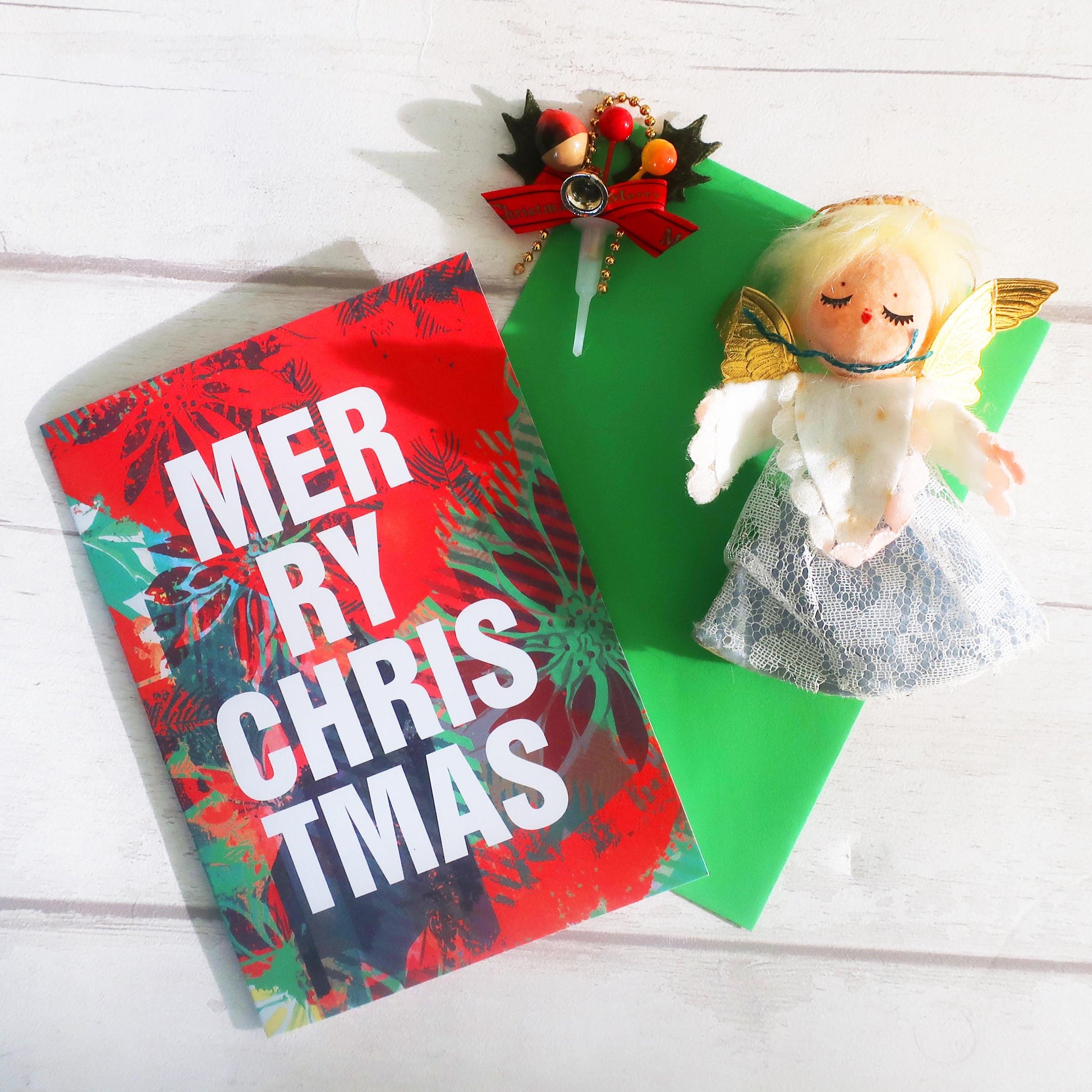 Christmas card with 'Merry Christmas' text, decorative bow, and angel figurine on a white wooden surface.