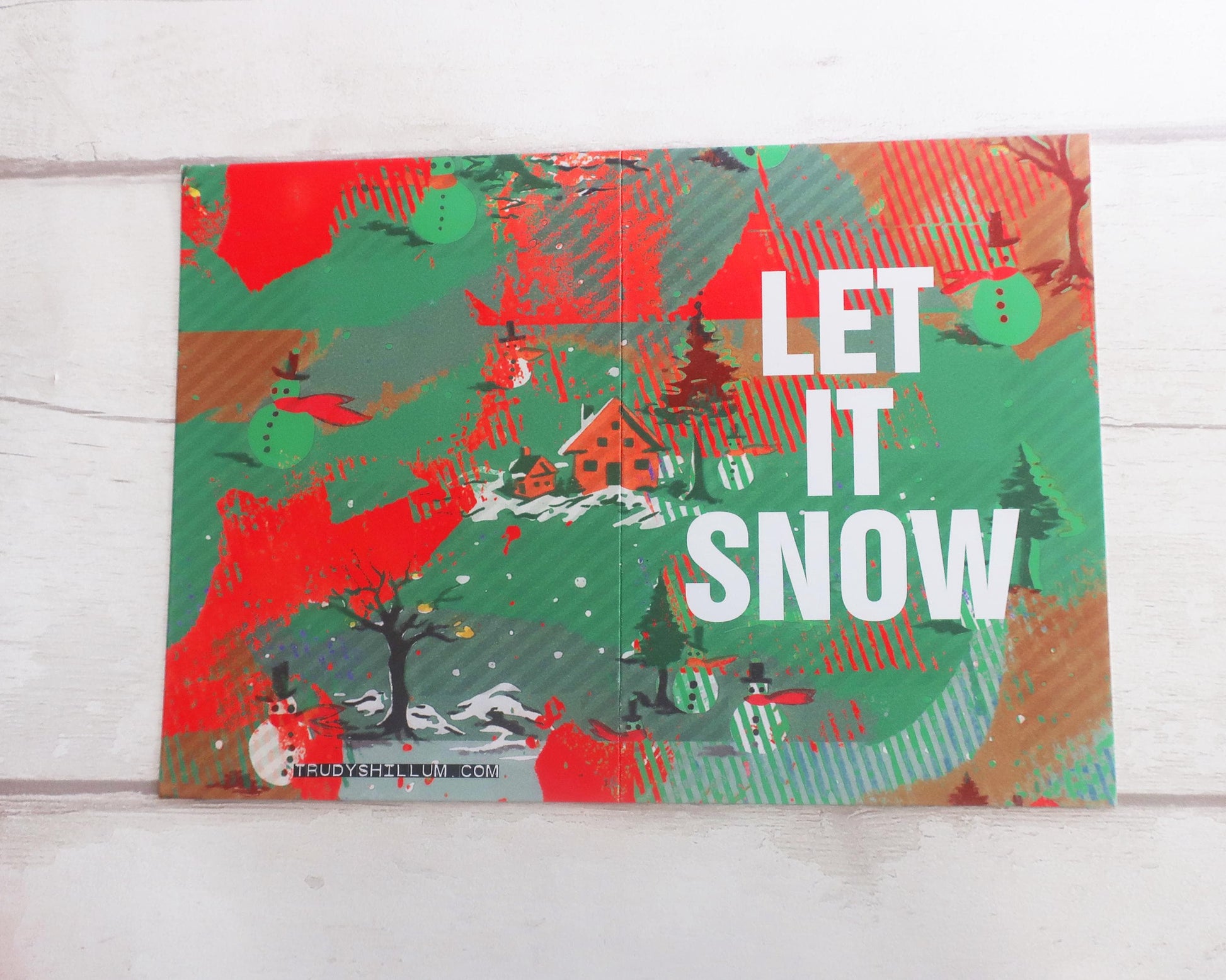 Decorative card with winter scene and 'Let It Snow' text on a wooden surface