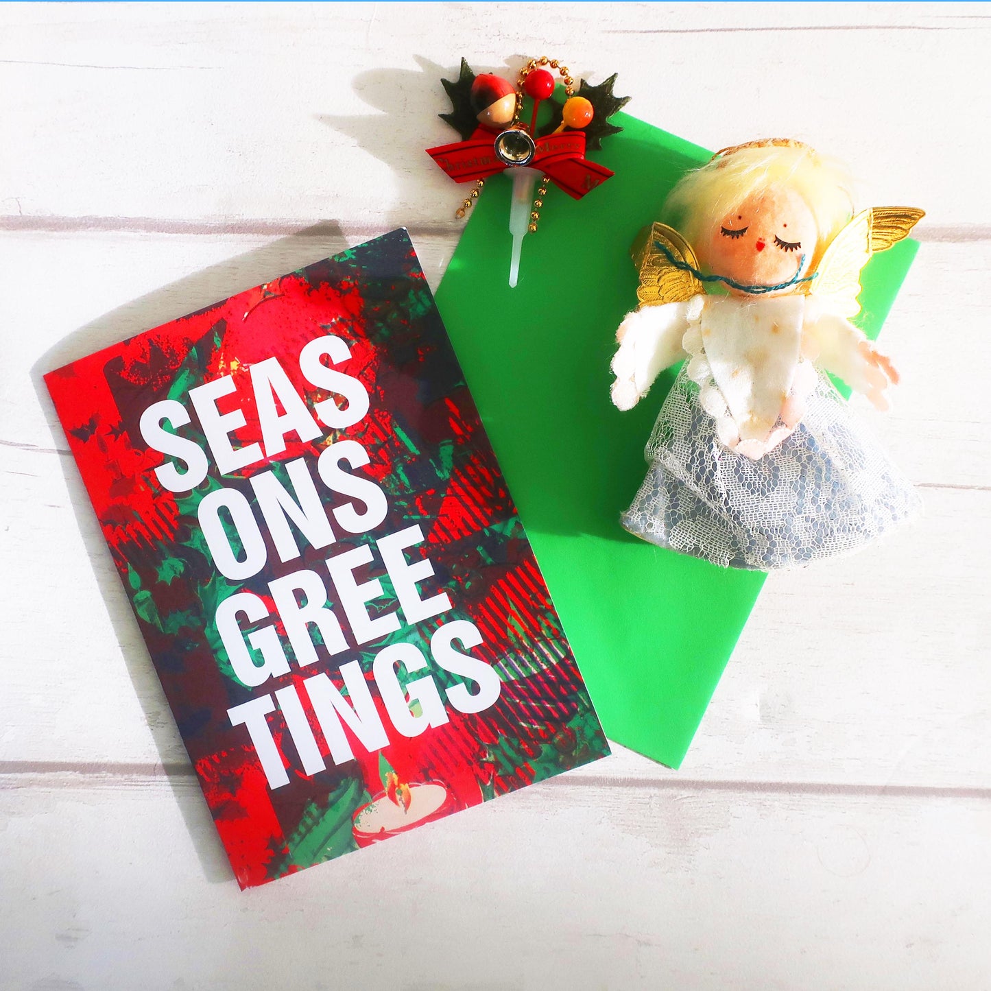 Christmas card with 'Seas onsgree tings' text, small angel figurine, and decorative item on a white surface.