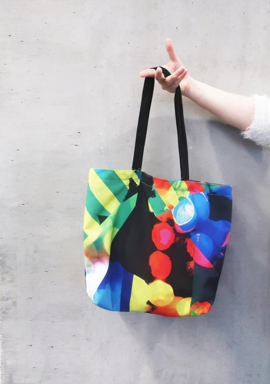 Colorful tote bag with black handles held by a person on a gray surface