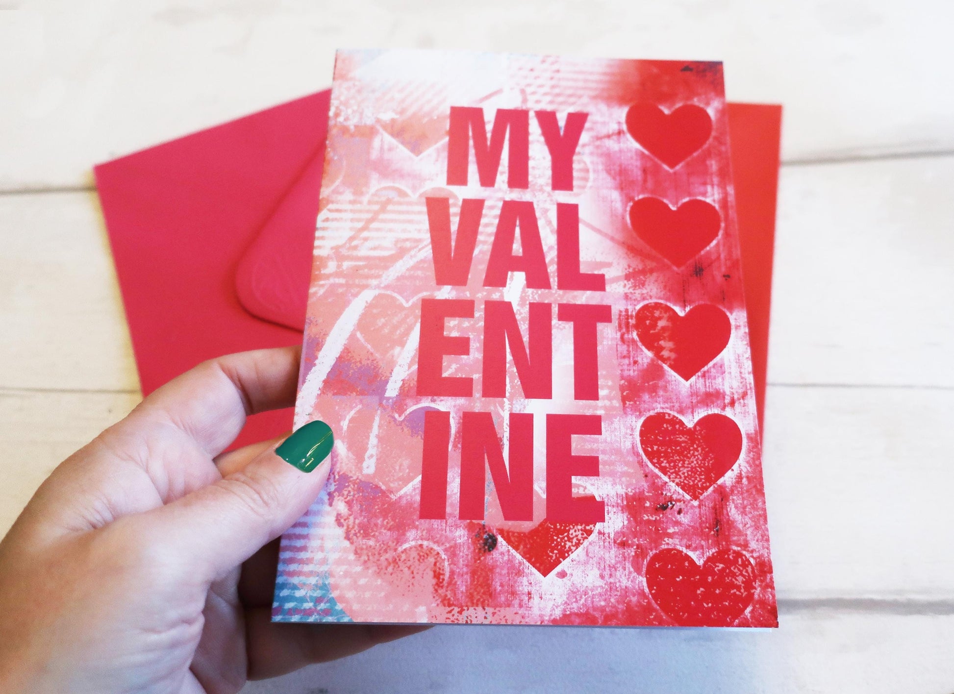 Hand holding a Valentine's Day card with hearts and 'My Valentine' text on a wooden surface.