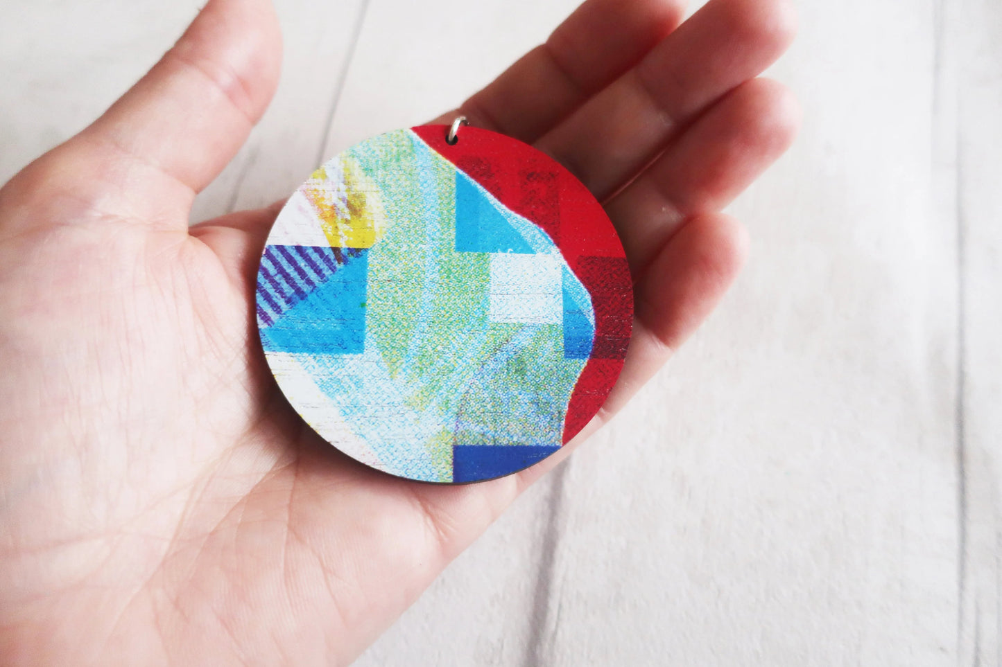 Colorful circular pendant held in a hand against a white background