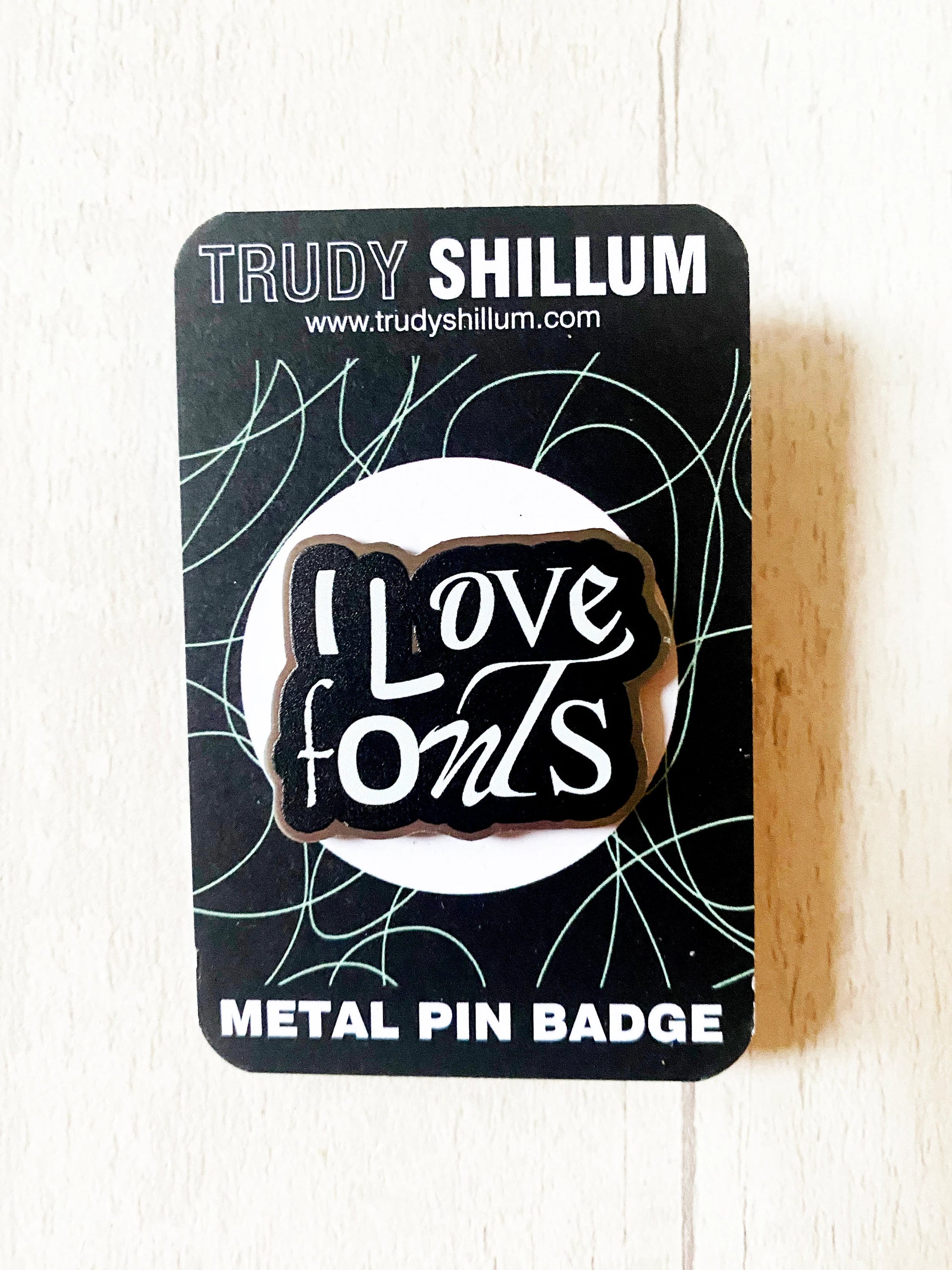 Metal pin badge with 'I Love Fonts' design on a Trudy Shillum branded card.