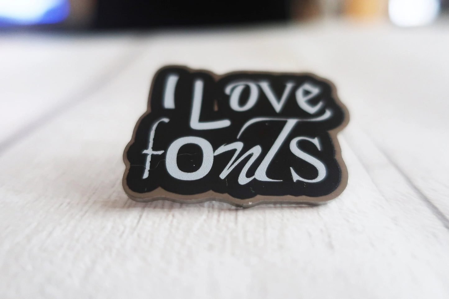 Pin with 'I Love Fonts' text on a wooden surface