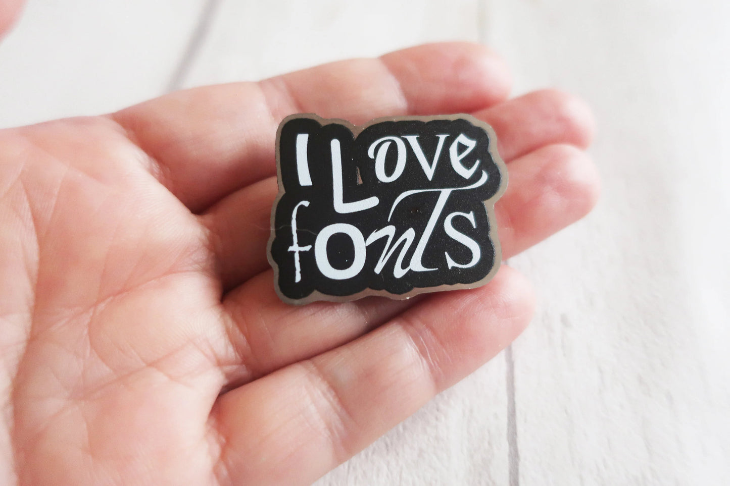 Pin with 'I Love Fonts' text held in a hand against a white background