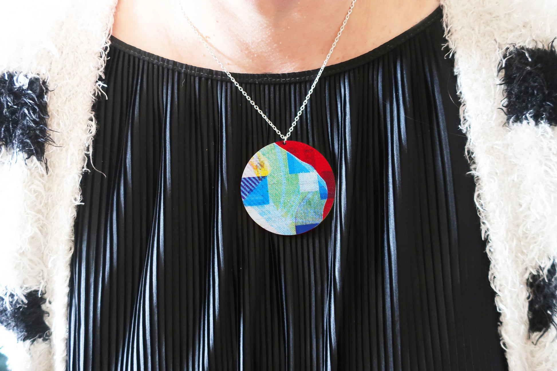 Person wearing a colorful pendant necklace with a black pleated dress.