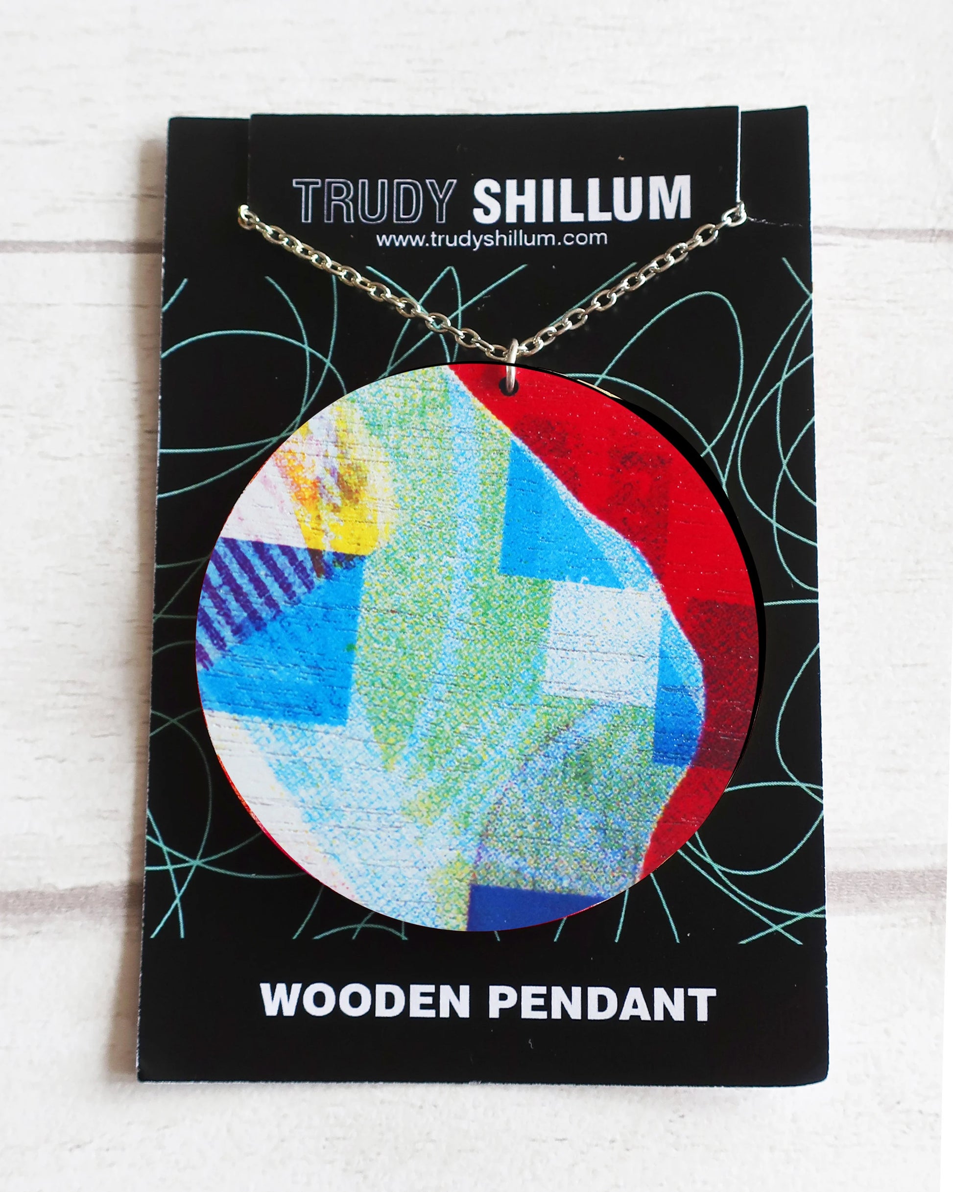 Colorful wooden pendant on a Trudy Shillum branded card against a white background