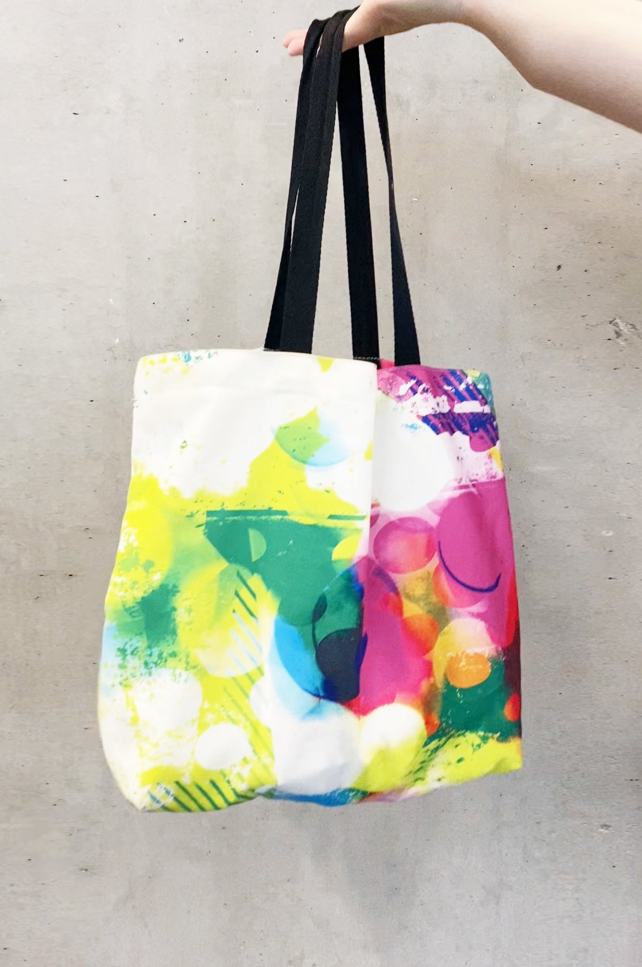 Colorful tote bag with abstract design held by a hand on a light gray background