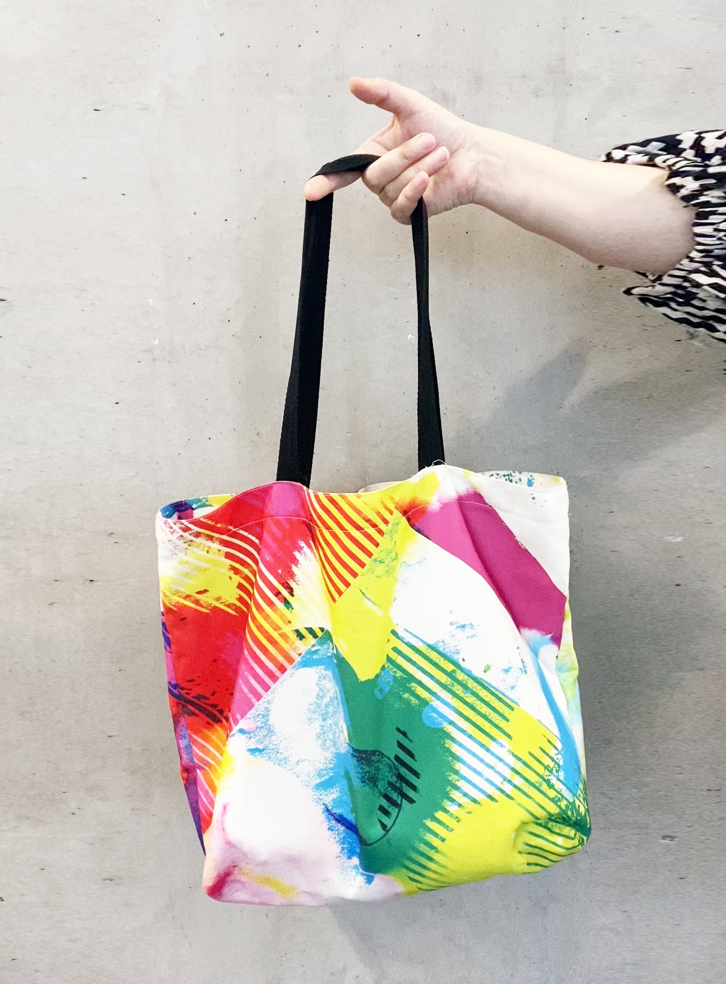Colorful tote bag with abstract design held by a hand against a plain background